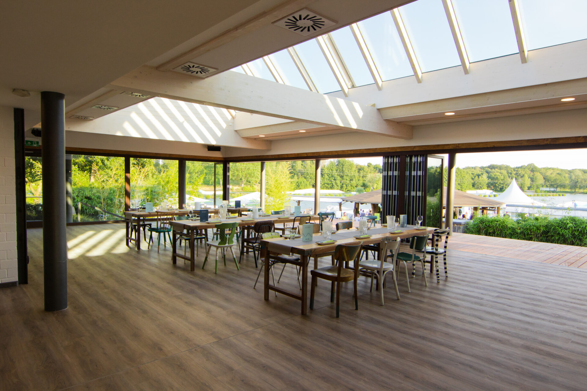 Eventraum mit drei eingedeckten Tischen, geöffneter Glasfront und Blick auf das dahinterliegende Gelände bei Sonne