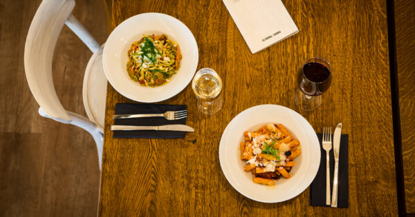 Draufsicht eines gedeckten Tisches mit zwei Pastagerichten und zwei gefüllten Weingläsern