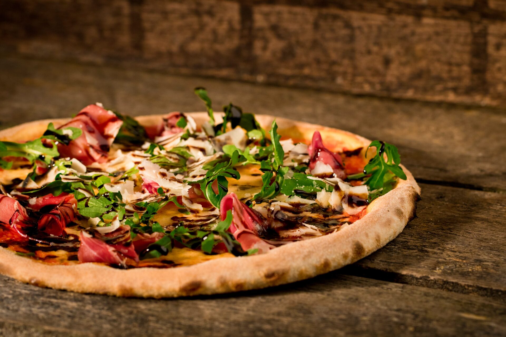 Nahaufnahme einer Pizza mit Schinken, Rucola und Balsamico