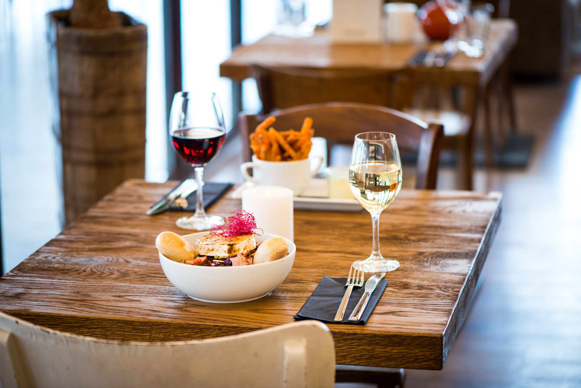 Tisch im Seehaus mit zwei gefüllten Weingläsern, dem Ziegenkäse Salat und Süßkartoffelpommes