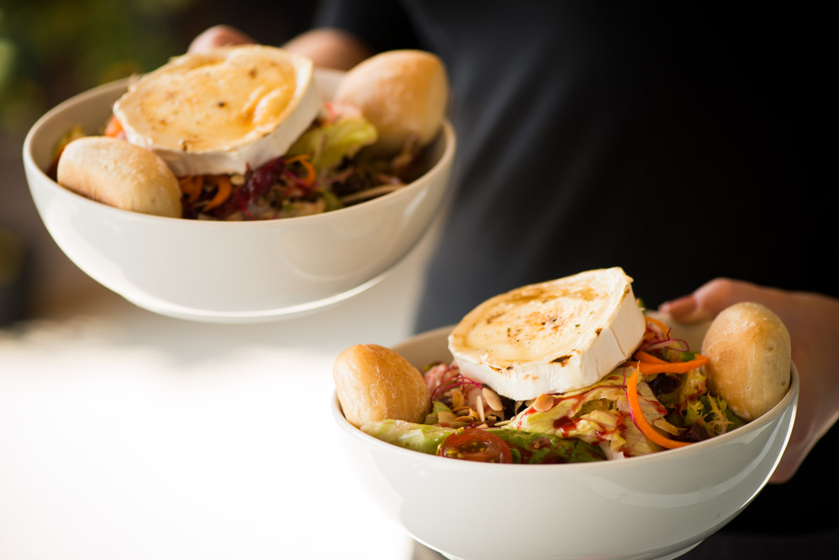 Nahaufnahme eines Kellners der zwei Ziegenkäse Salate trägt