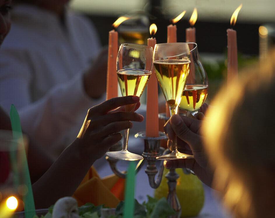 Leute stoßen mit Weingläsern auf einem schwimmenden Grillplatz an bei Sonnenuntergang und Kerzenschein